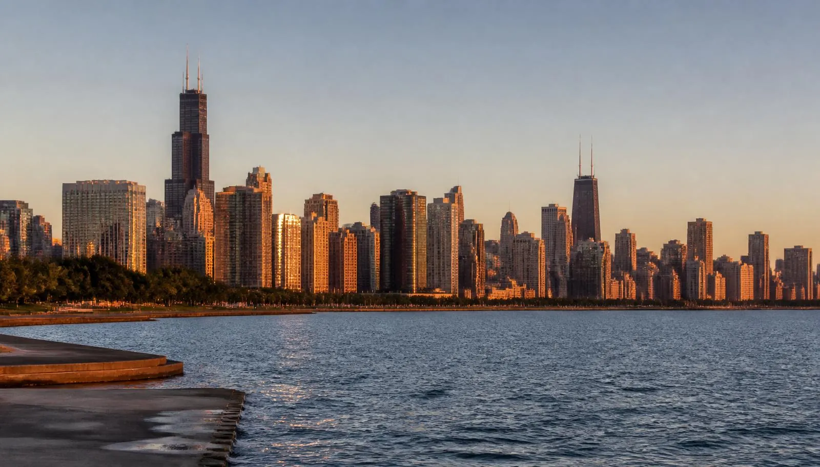 The Chicago skyline with Willis Tower and the John Hancock Center glowing at golden hour above Lake Michigan seen from the lakefront