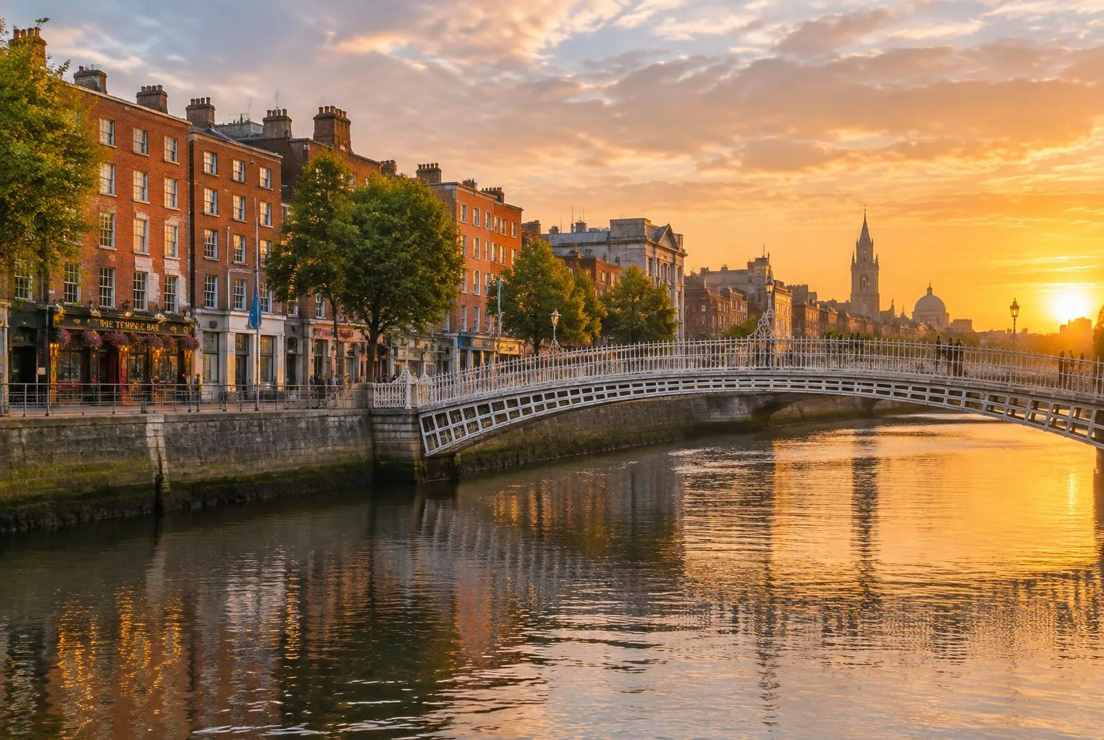 The white Ha'penny Bridge arching over the River Liffey in Dublin, Ireland at golden hour, with red-brick Georgian buildings along the quays